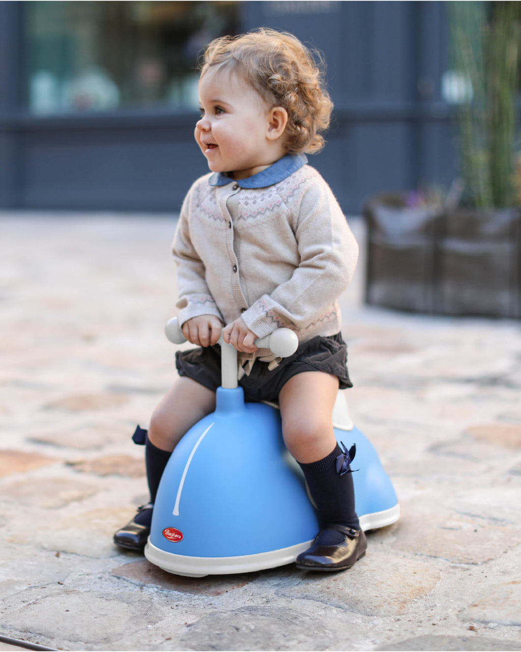 Child sitting on a blue baghera twister on a stone pavement