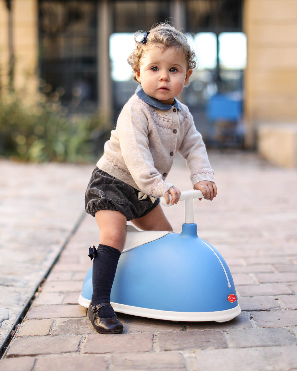 Child riding a blue bagher twiseter ride-on toy on a paved path.