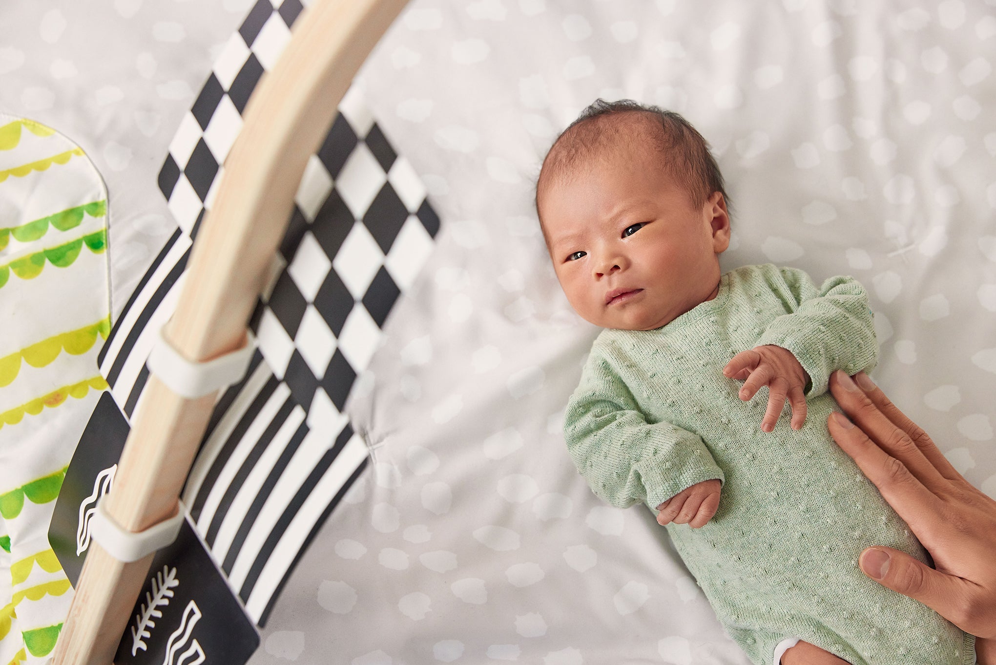 Newborn baby in a green onesie lying on a white blanket with a black and white striped blanket looking at lovevery black and white cards.