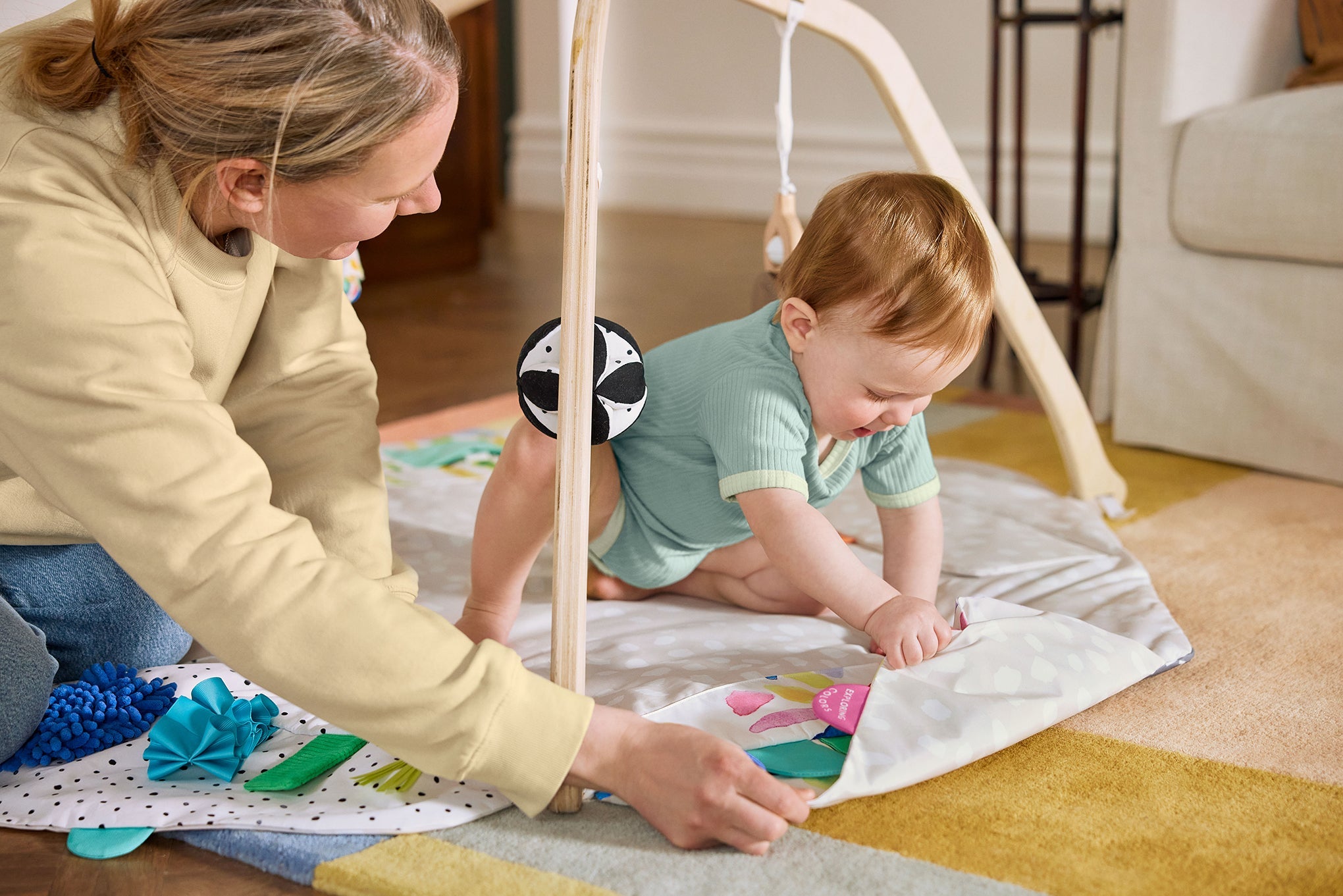 Woman and baby playing on a mat with toys in a home setting