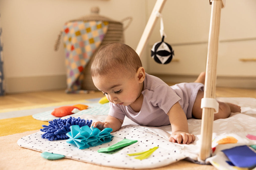 Child playing with toys on a mat in a room with a tepee and colorful blanket.