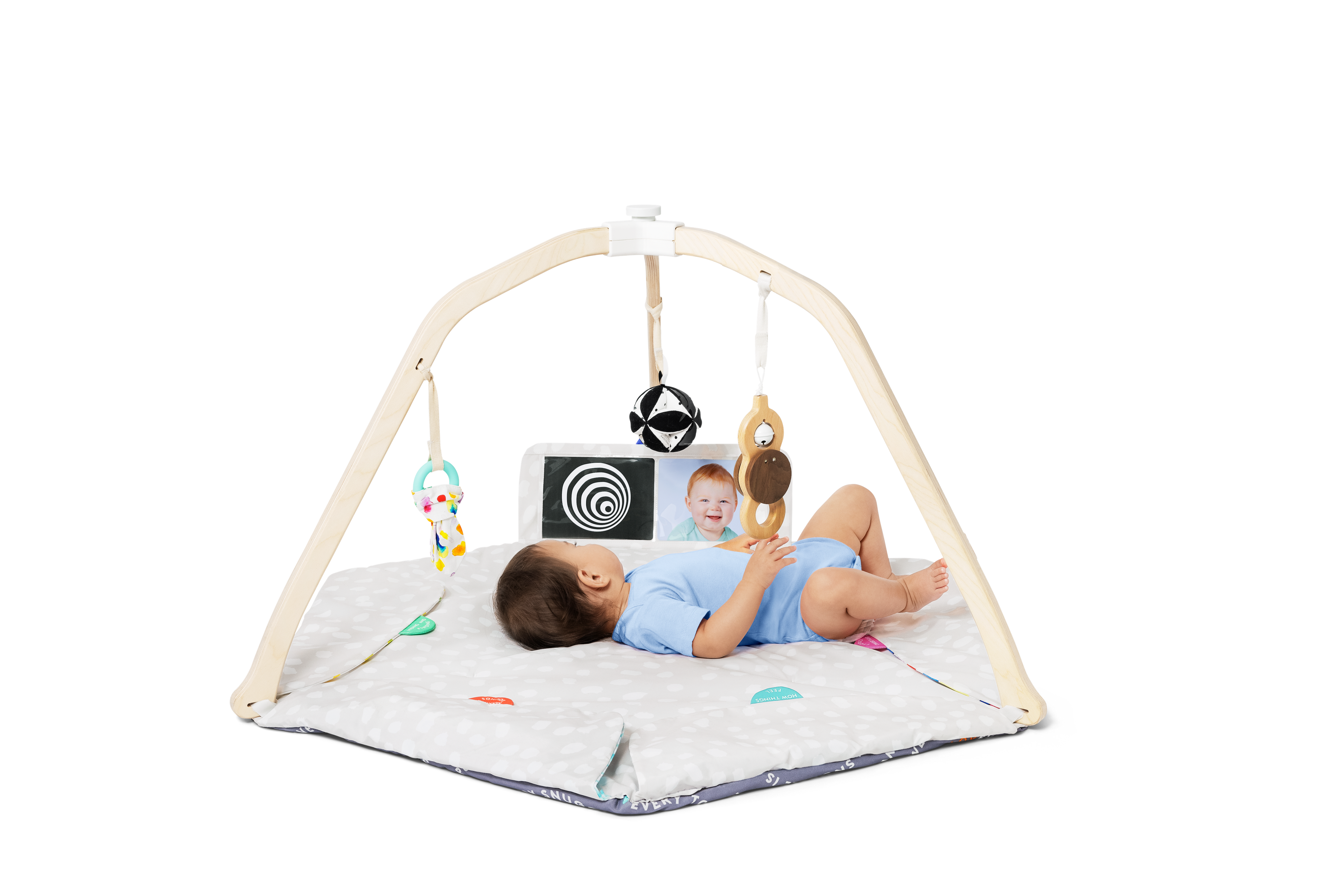 Baby lying on a play mat with a baby gym and toys on a white background