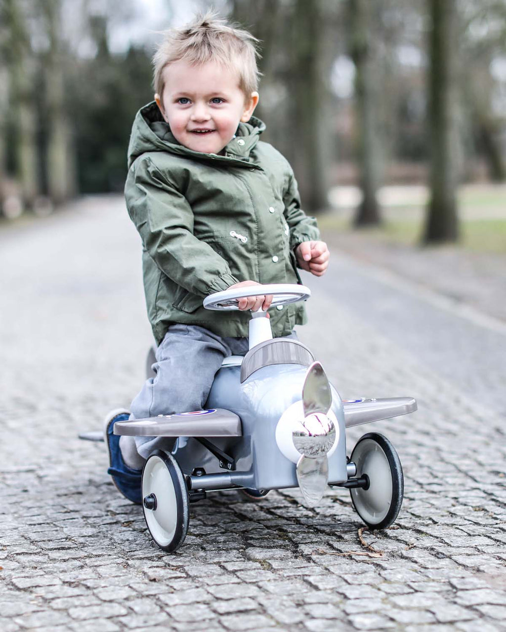 Child riding a toy airplane on a paved path with trees in the background