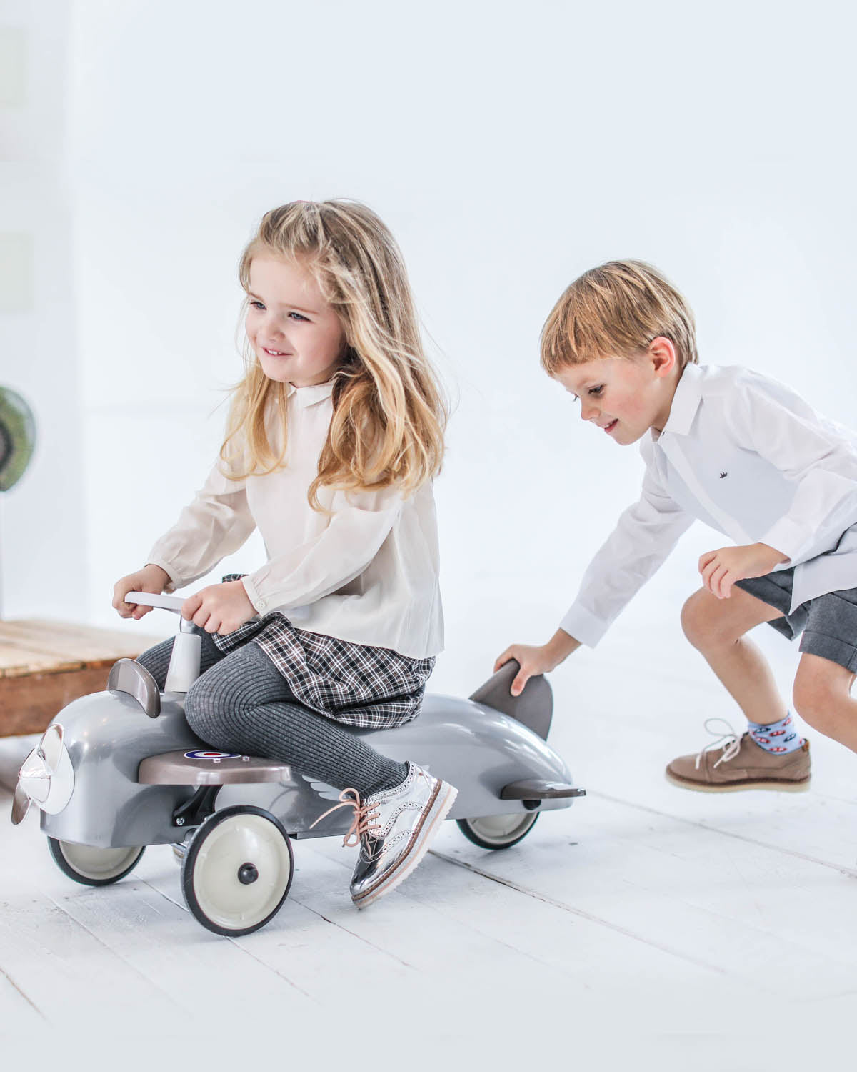 Two children playing with a baghera toy airplane car on a white floor.