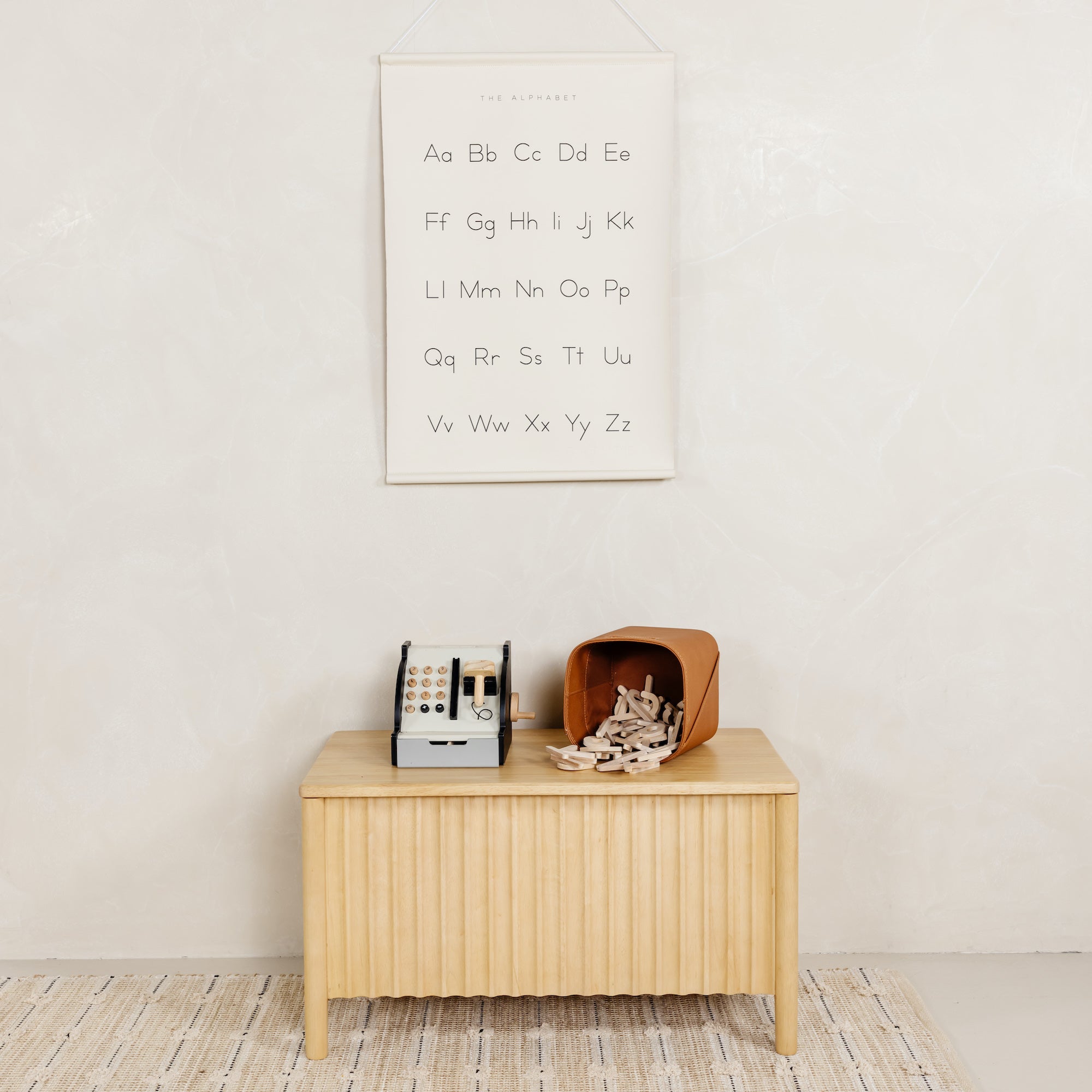 Wooden cabinet with decorative items against a white wall with a alphabet poster.