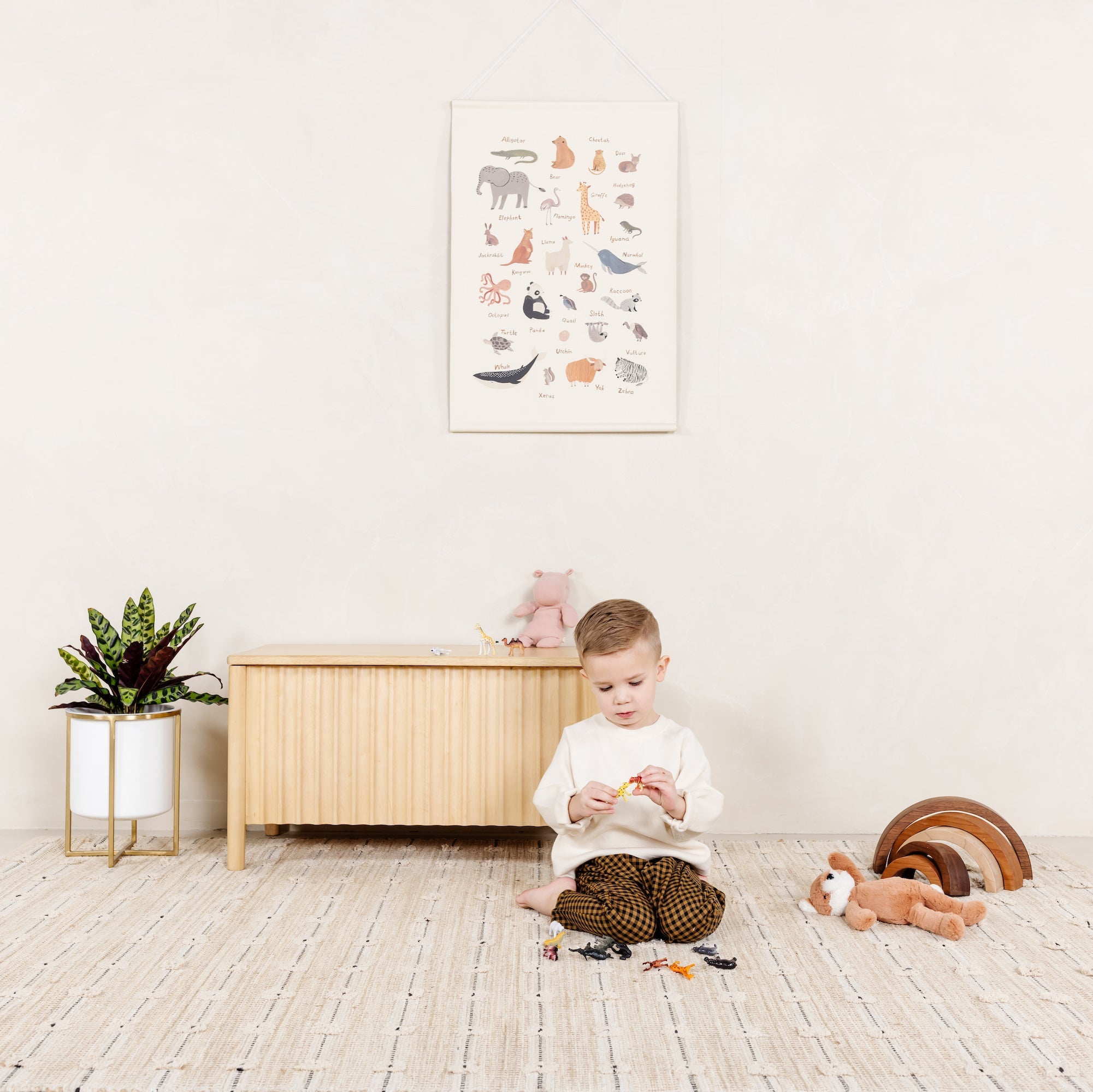 Child playing with toys on a wooden floor in a room with a white wall and a cabinet.