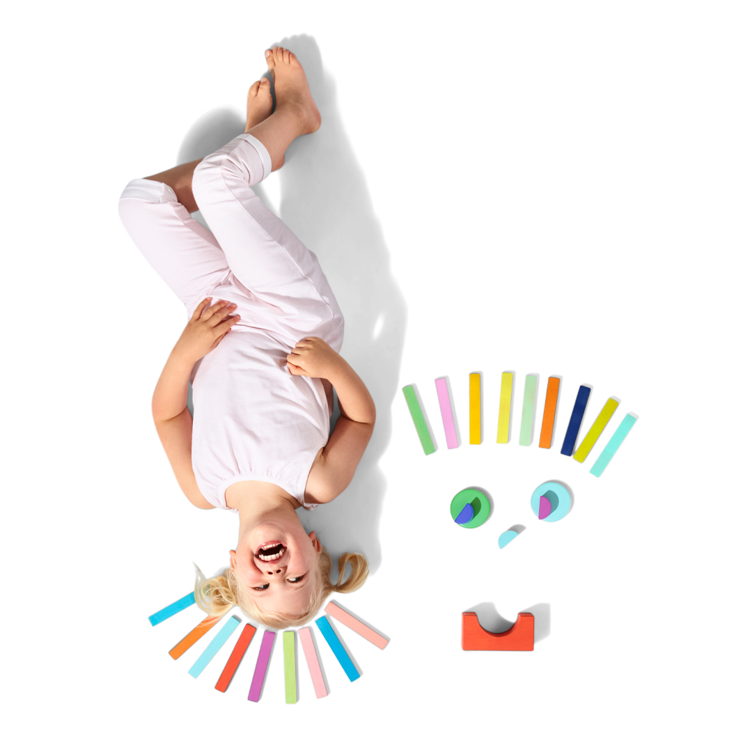 Child lying on a white surface with colorful wooden blocks from lovevery around