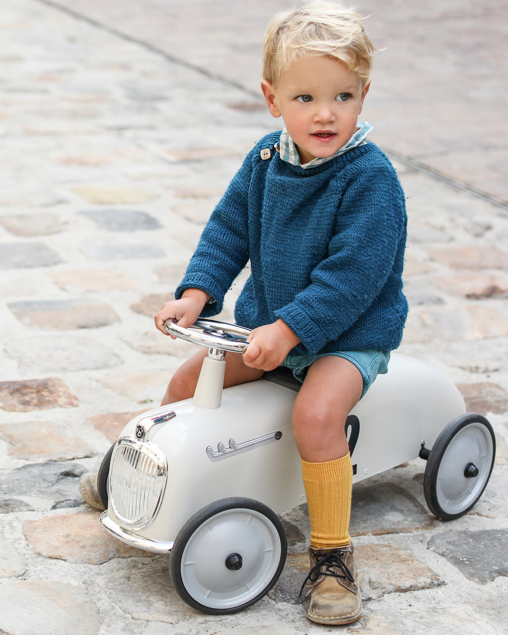 Child sitting on a toy car on a stone pavement