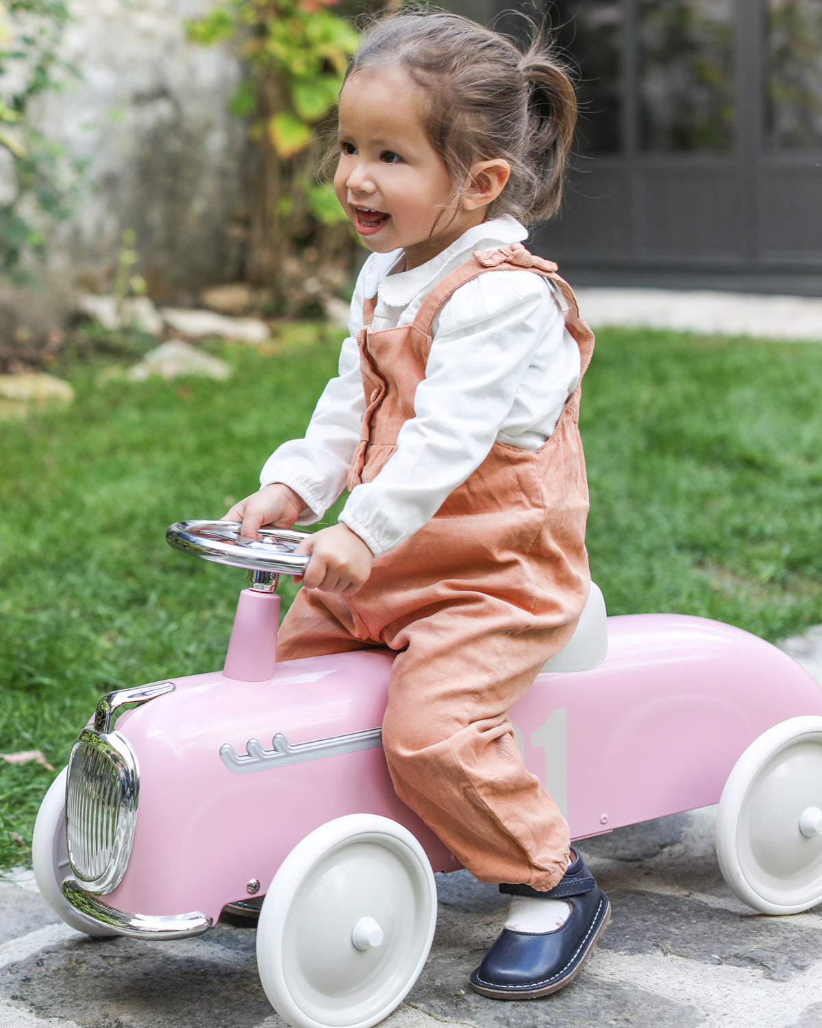 child riding a Pink baghera ride-on roadster with the number 01 in a garden setting