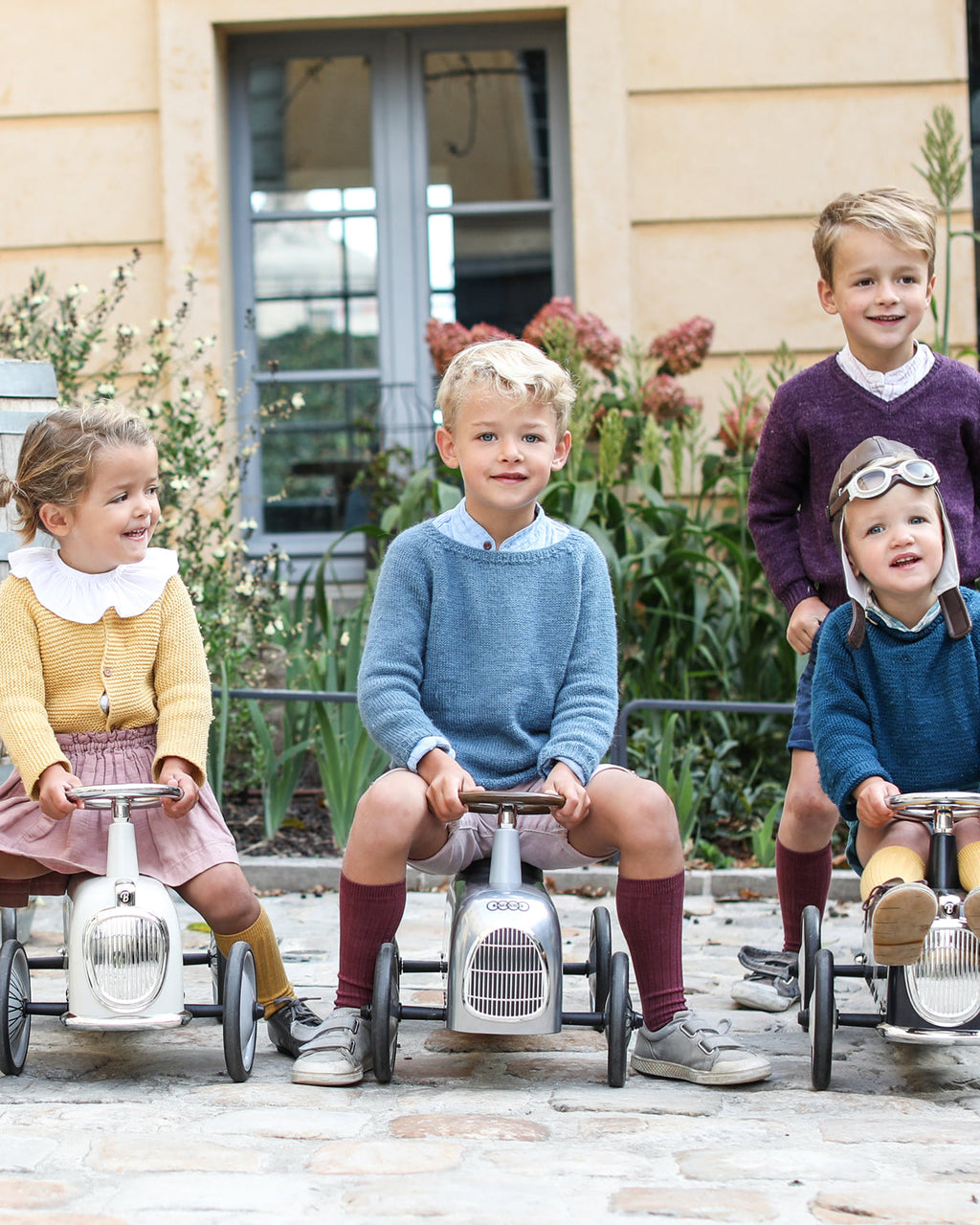 Four children on vintage-style baghera ride-on cars in a garden setting
