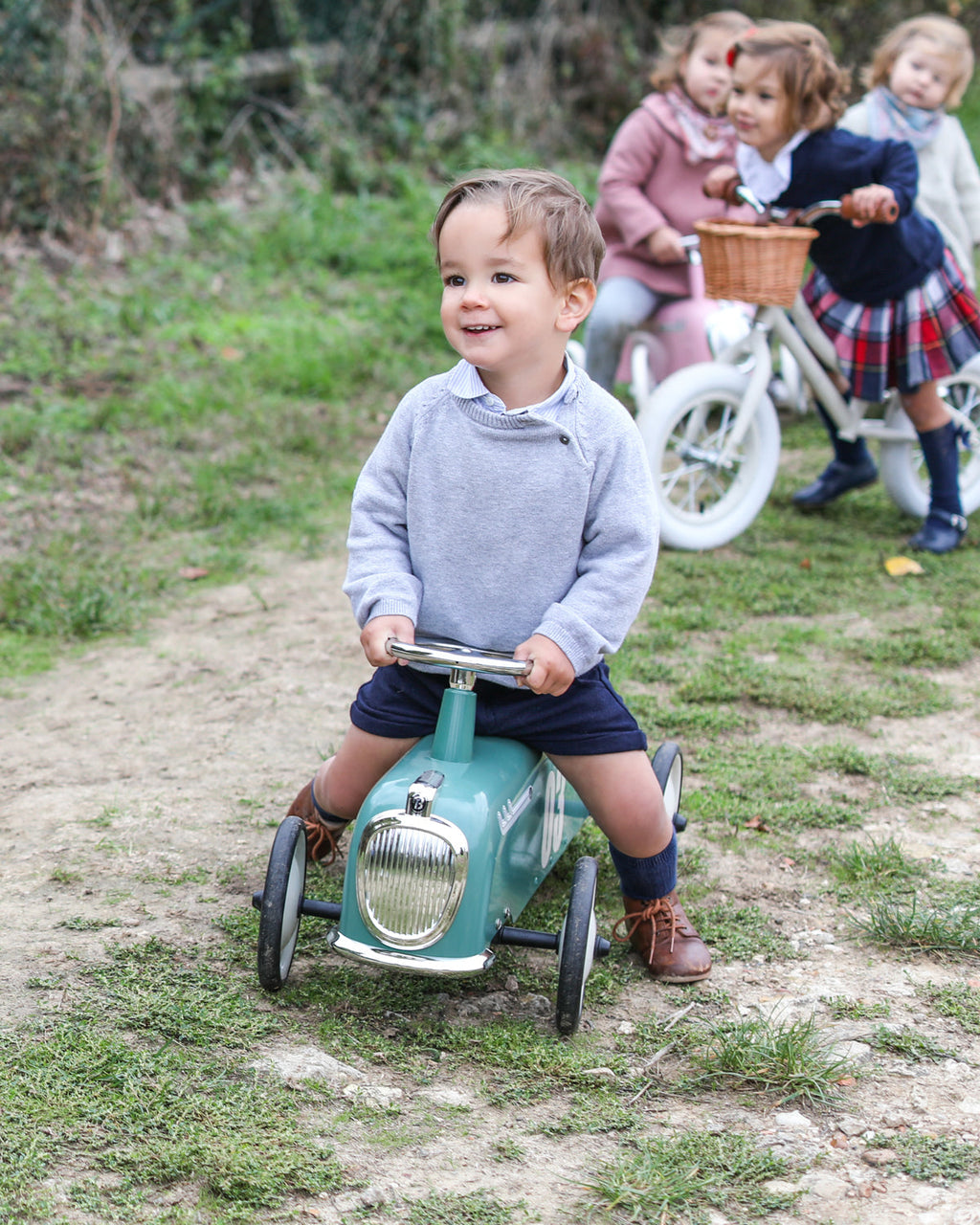 Child riding a toy car outdoors with other children in the background