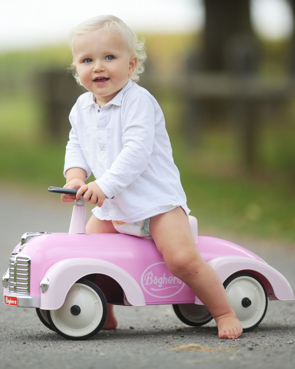 Child sitting on a pink baghera speedster toy car outdoors