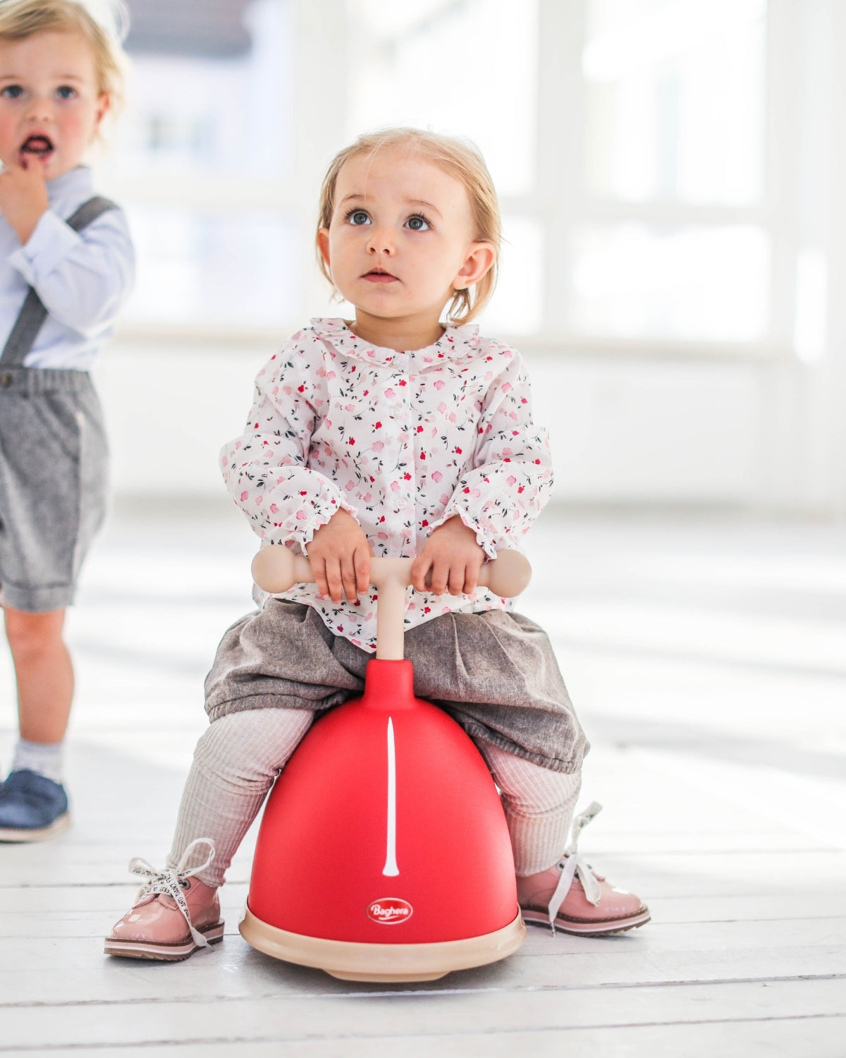 Two children playing with a red baghera twister on a light wooden floor.