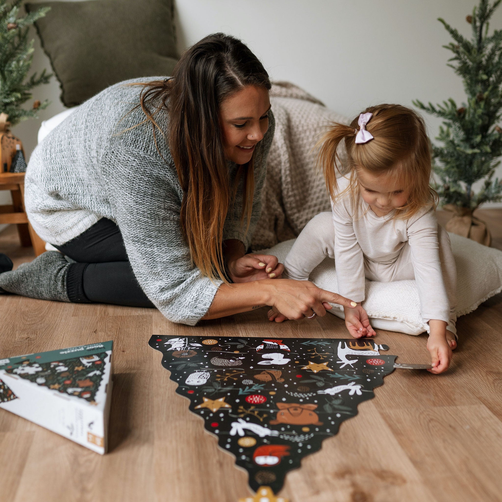 Woman and child interacting with a Christmas tree-shaped calendar on a wooden floor.