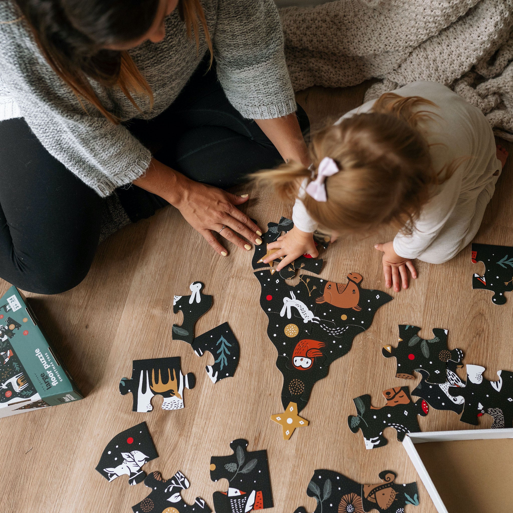 Woman and child playing with a puzzle on a wooden floor