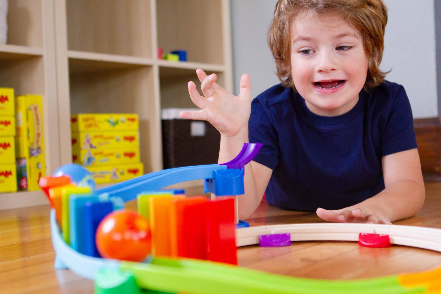 Boy playing with Haba Kullerbu Kringel Domino Play Track Starter Set a colorful toy track set with. ashelf on the background