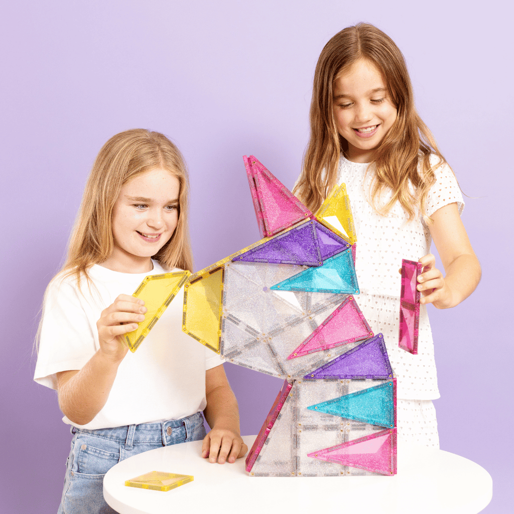 Two children playing with colorful geometric building blocks against a purple background