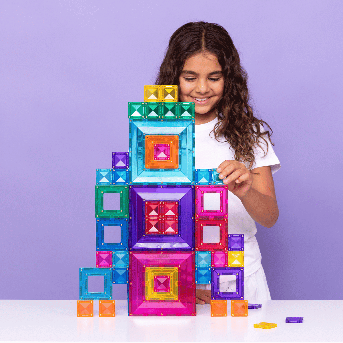 Child playing with colorful magnetic building blocks against a purple background