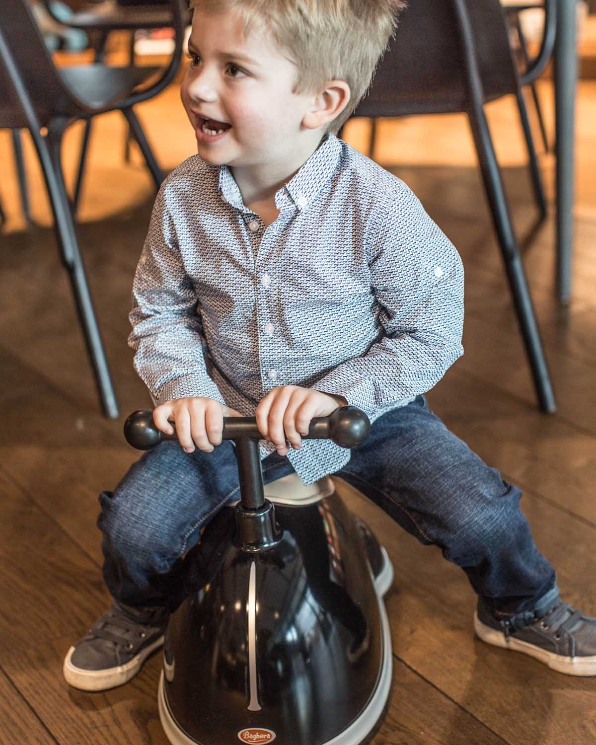 Child riding a black baghera twister indoors on a wooden floor.