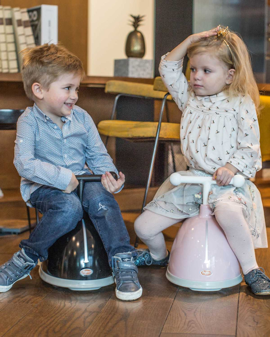 Two children sitting baghera twisters  in a room with wooden flooring.